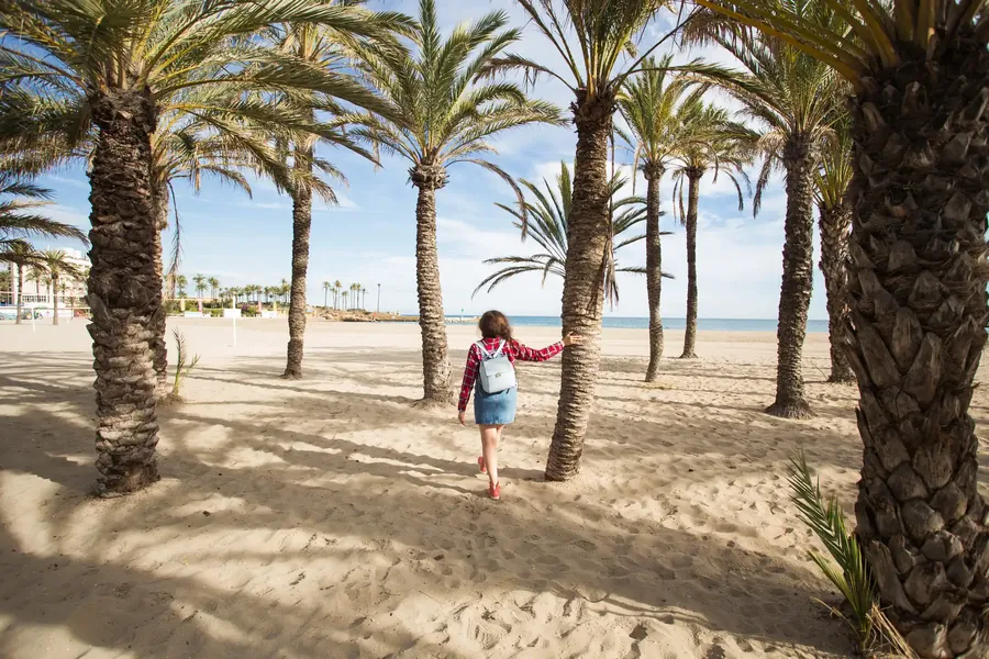 Una mujer camina por una ancha playa de arena bordeada de cocoteros