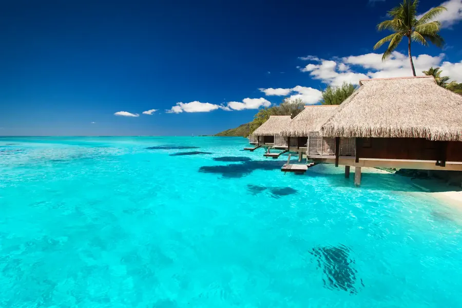 Villas de playa entre palmeras con escaleras a una laguna turquesa en Maldivas
