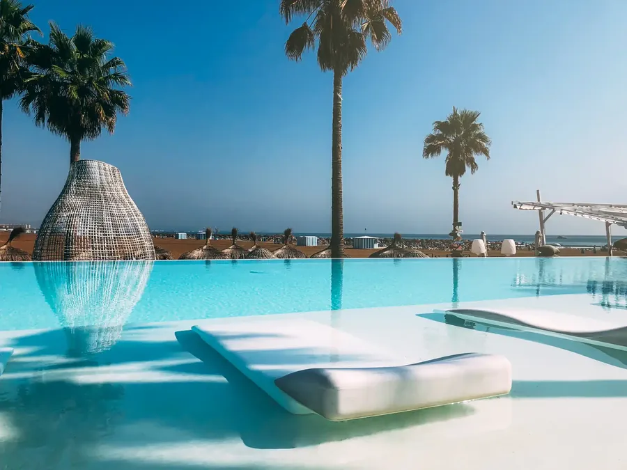 Una piscina de resort en una playa bordeada de palmeras altas