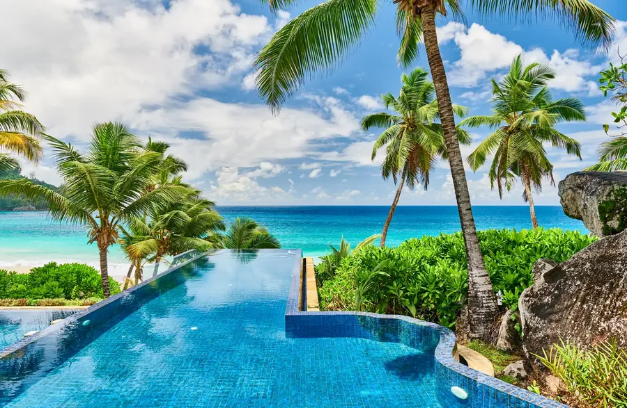 Una piscina de resort bajo palmeras junto a una playa blanca en Seychelles