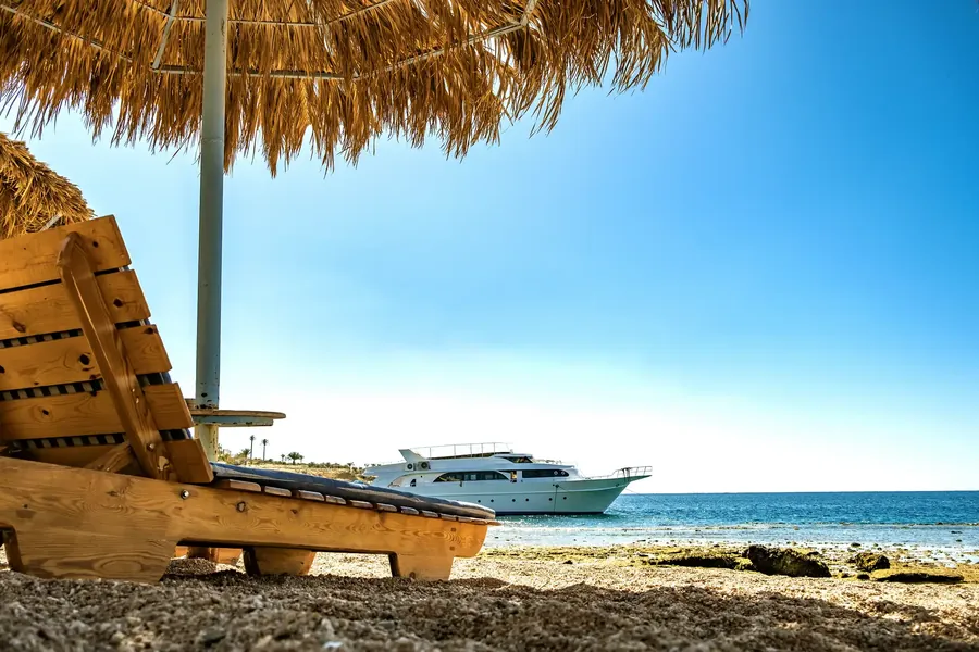 Tumbonas de madera bajo una sombrilla de paja en una playa blanca