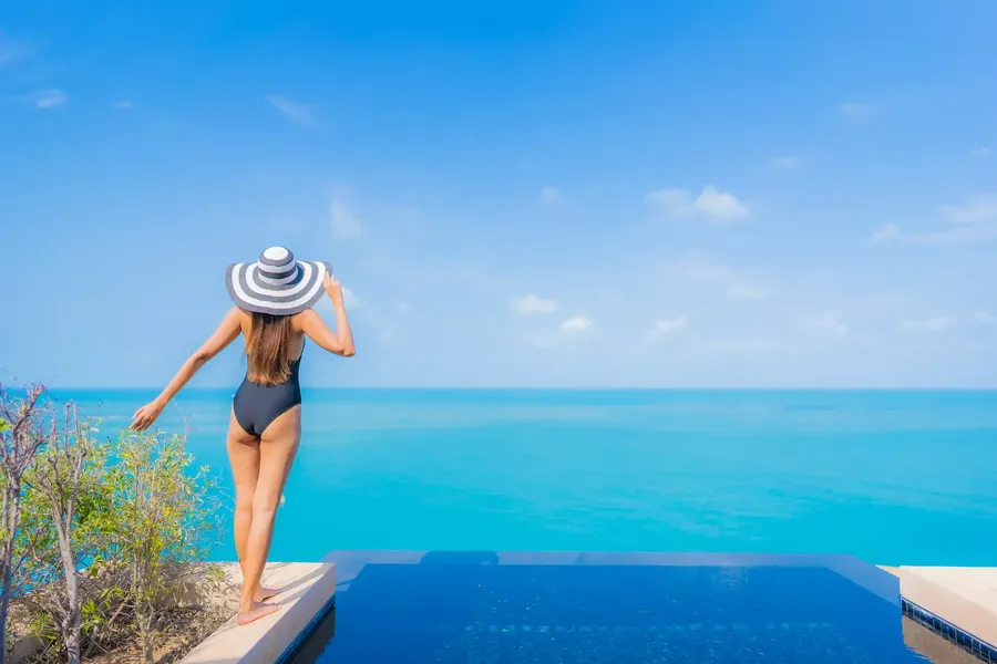 Una mujer con sombrero de rayas mira el mar desde una piscina