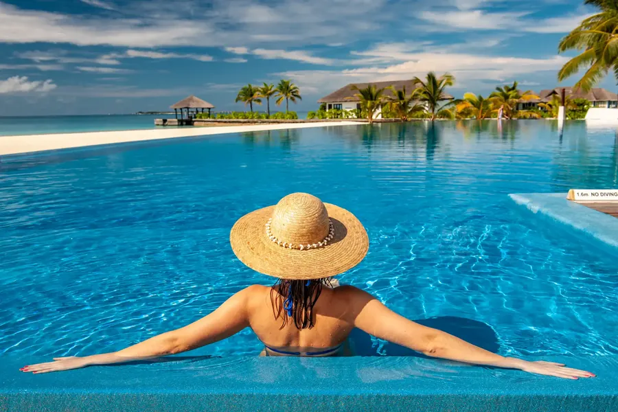 Una mujer con sombrero de paja en una piscina frente a una laguna